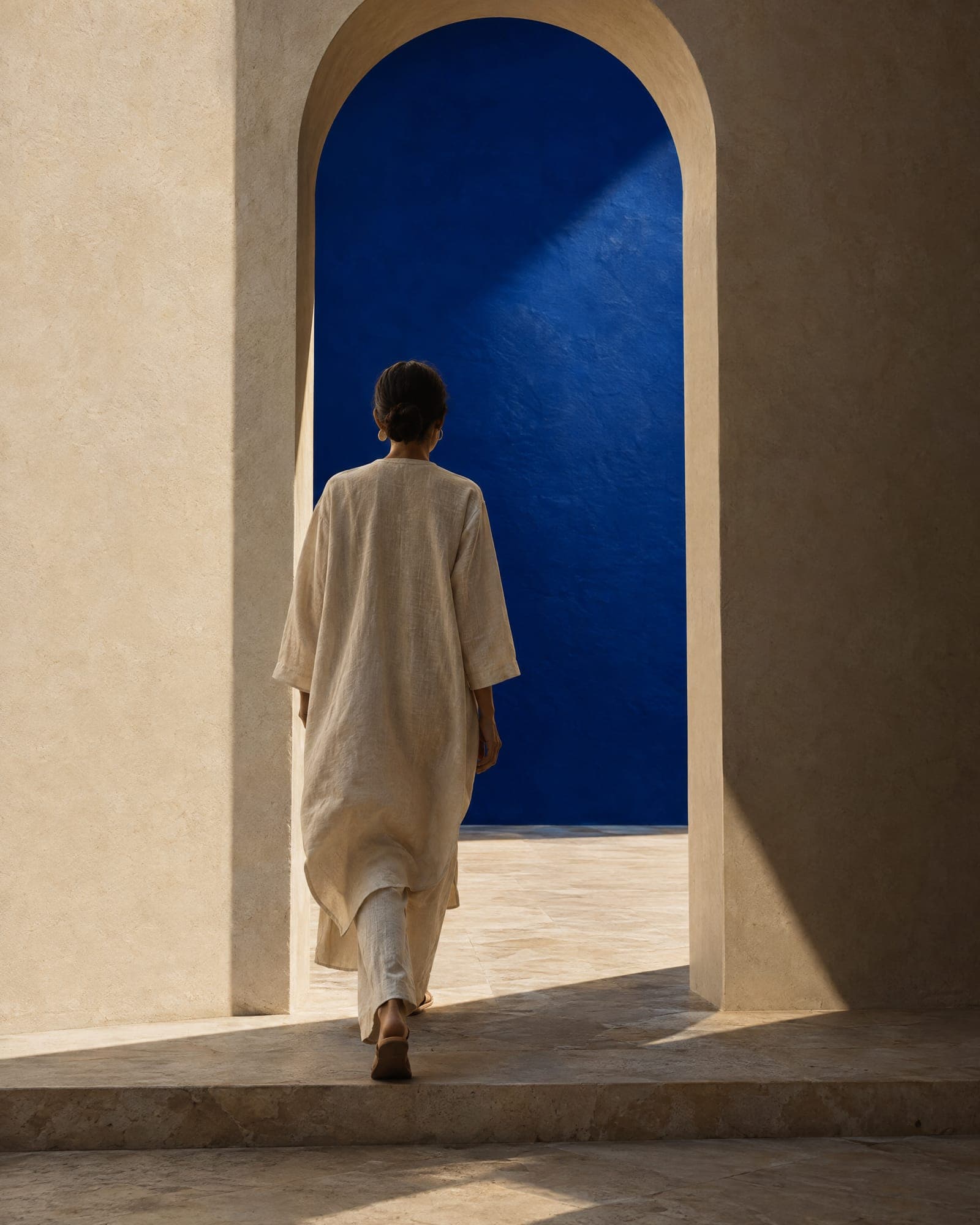 A figure framed by an arch, stepping onto pale stone, back to camera